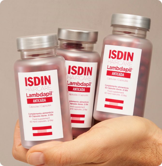 Botes de Lambdapil Cápsulas Anticaída de ISDIN sostenidos en una mano, tratamiento de apoyo para el cuidado del cabello en invierno.