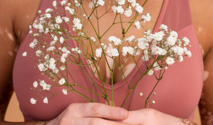 Mujer sosteniendo pequeñas flores blancas frente al pecho como símbolo de cuidado y conexión con el cuerpo.