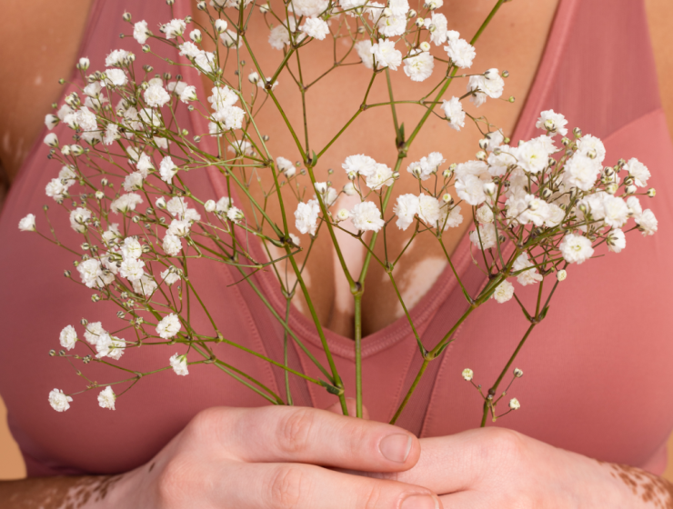 Mujer sosteniendo pequeñas flores blancas frente al pecho como símbolo de cuidado y conexión con el cuerpo.