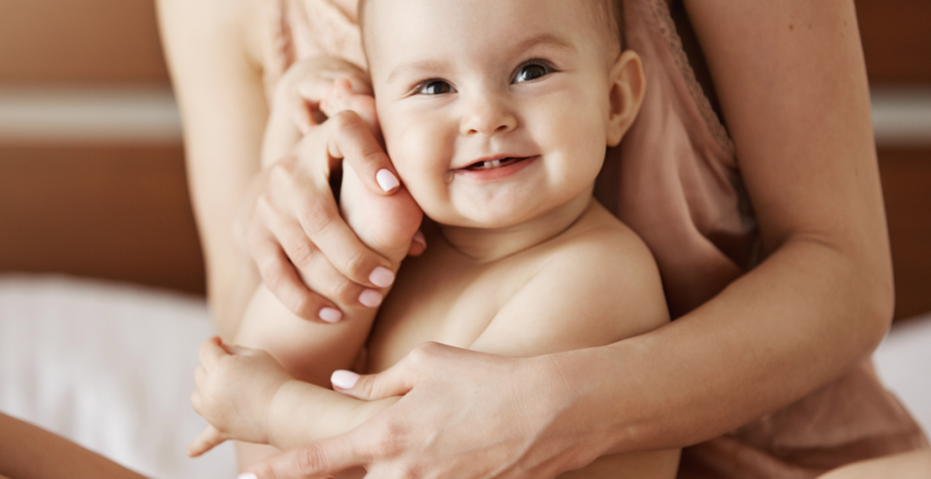Bebé con piel suave y saludable en brazos de su madre, representando los beneficios de una buena hidratación.