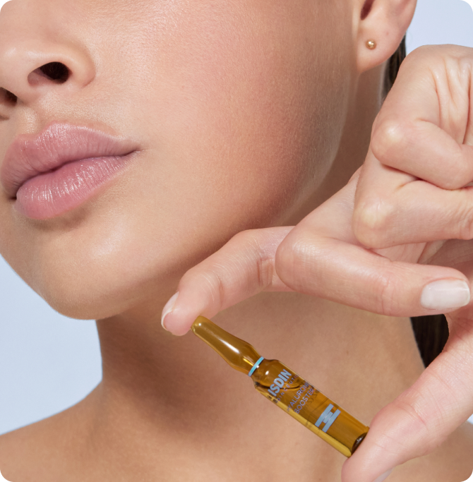 Primer plano de piel del rostro y mano sosteniendo una ampolla de vidrio ámbar de ácido hialurónico isdin