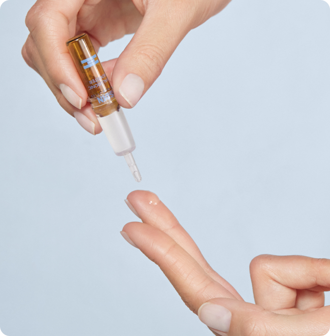 Mano aplicando sérum transparente con cuentagotas sobre la yema de los dedos, fondo claro. Producto ISDIN Hyaluronic Booster, textura ligera para hidratar y dar brillo natural antes de fiestas y eventos.