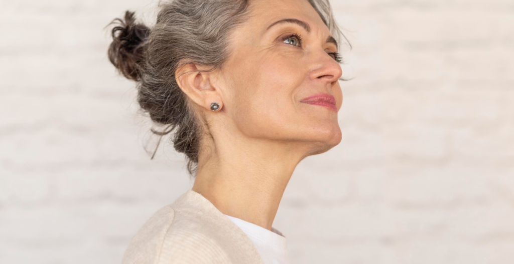 Mujer adulta con canas mirando hacia arriba con actitud serena, representando bienestar y confianza durante la etapa de la menopausia.