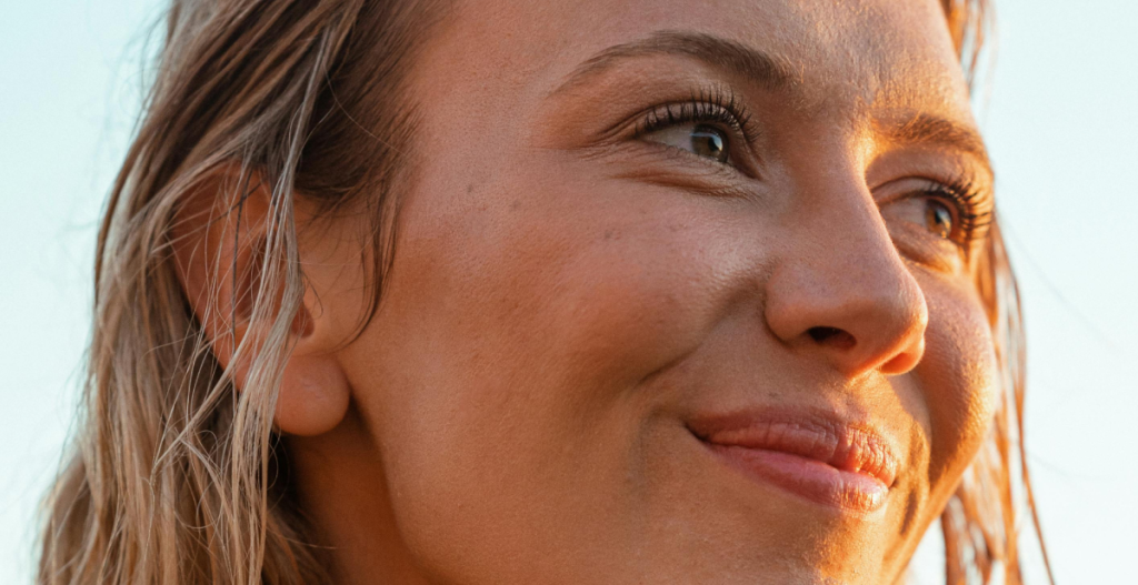 Primer plano de una mujer con piel uniforme y luminosa al atardecer, resultado del uso de tratamientos con niacinamida y vitamina C.