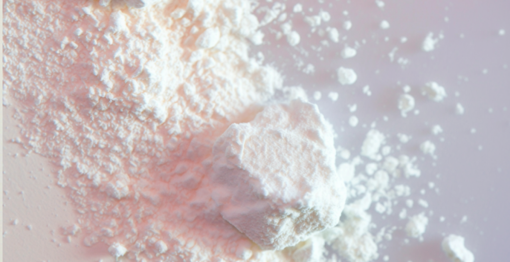 Textura en polvo clara con matices rosados, inspirada en formulaciones con niacinamida y ácido tranexámico.