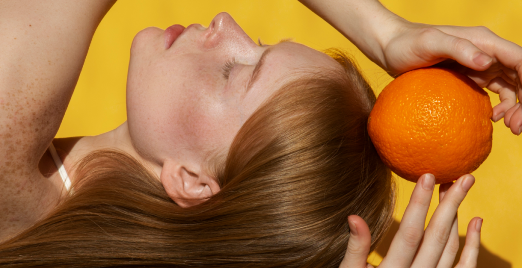 Mujer con piel luminosa sosteniendo una naranja, símbolo de la vitamina C y sus beneficios para la piel