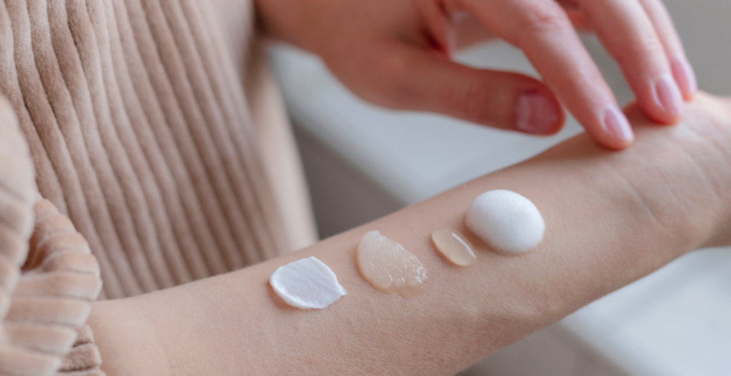 Diferentes texturas de productos cosméticos (crema, gel, aceite y espuma) aplicadas en un brazo, representando los pasos del skin cycling