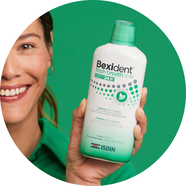 Primer plano de Bexident Fresh Breath colutorio sostenido en la mano sobre fondo verde.