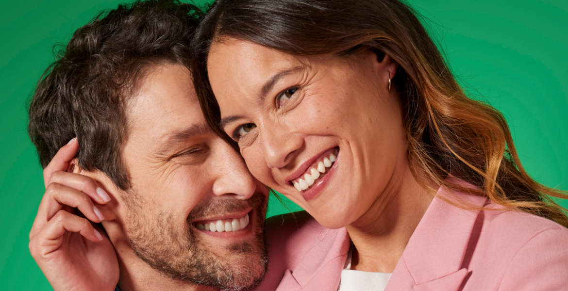 Pareja sonriendo de cerca sobre fondo verde, transmitiendo frescor, seguridad y confianza al hablar.
