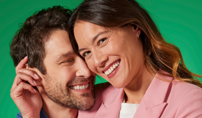 Pareja sonriendo de cerca sobre fondo verde, transmitiendo frescor, seguridad y confianza al hablar.