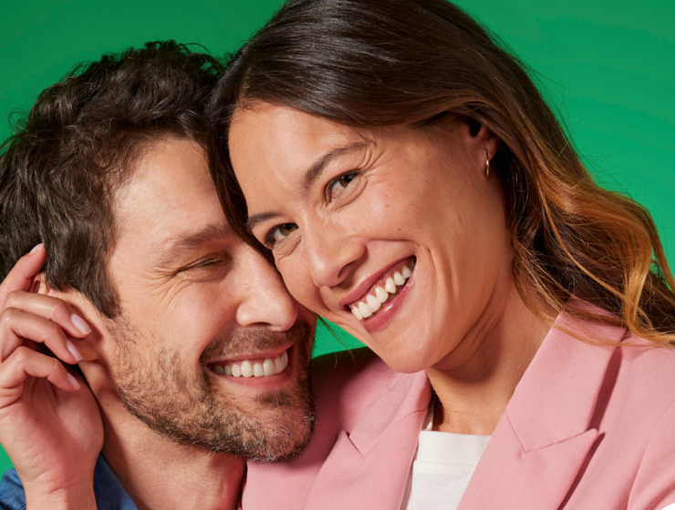 Pareja sonriendo de cerca sobre fondo verde, transmitiendo frescor, seguridad y confianza al hablar.