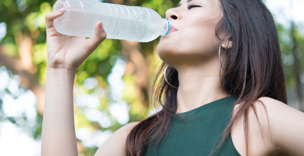 Mujer bebiendo agua para hidratarse y ayudar a mantener la boca fresca durante el día.