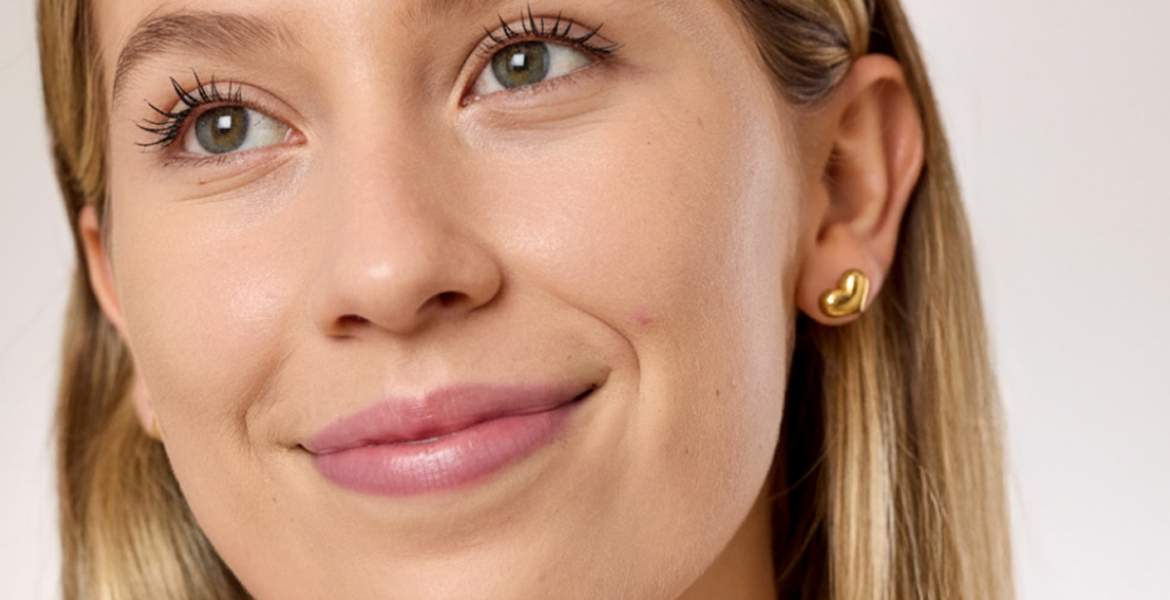 Primer plano de mujer joven de piel clara con acabado natural en la piel y pequeñas imperfecciones visibles en la mejilla.