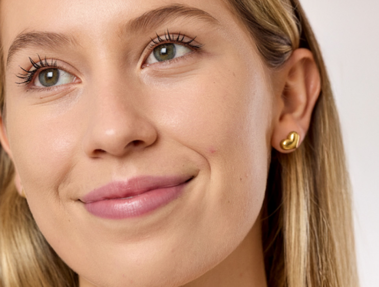 Primer plano de mujer joven de piel clara con acabado natural en la piel y pequeñas imperfecciones visibles en la mejilla.