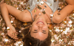 Mujer acostada boca arriba rodeada de confeti dorado, sonriendo a la cámara. Representa metas 2026, celebración de propósitos de Año Nuevo y skin goals.