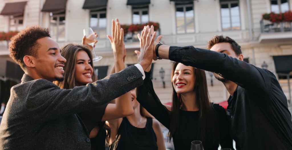 Grupo diverso de amigos sonriendo y chocando las manos al aire libre. Celebración de metas, propósitos de Año Nuevo 2026 y goal setting juntos
