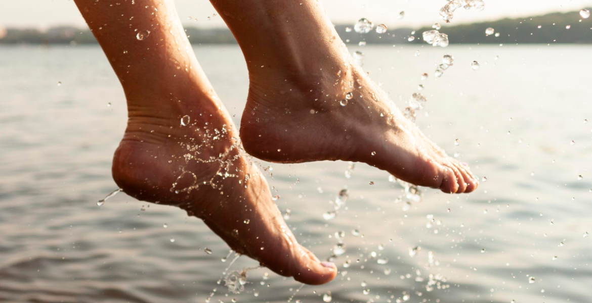 Pies descalzos saliendo del agua con gotas visibles, imagen que representa hidratación natural y cuidado de pies secos y talones agrietados