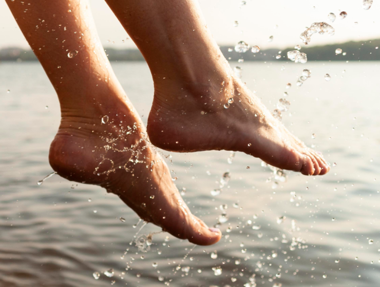 Pies descalzos saliendo del agua con gotas visibles, imagen que representa hidratación natural y cuidado de pies secos y talones agrietados