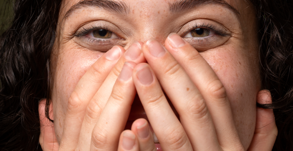 chica sonriendo mientras se tapa la cara con las manos