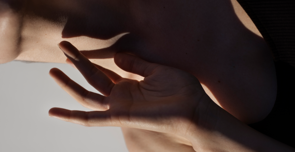 Mano tocando cuello iluminado por luz cálida que sugiere cuidado de la piel y conexión sensorial