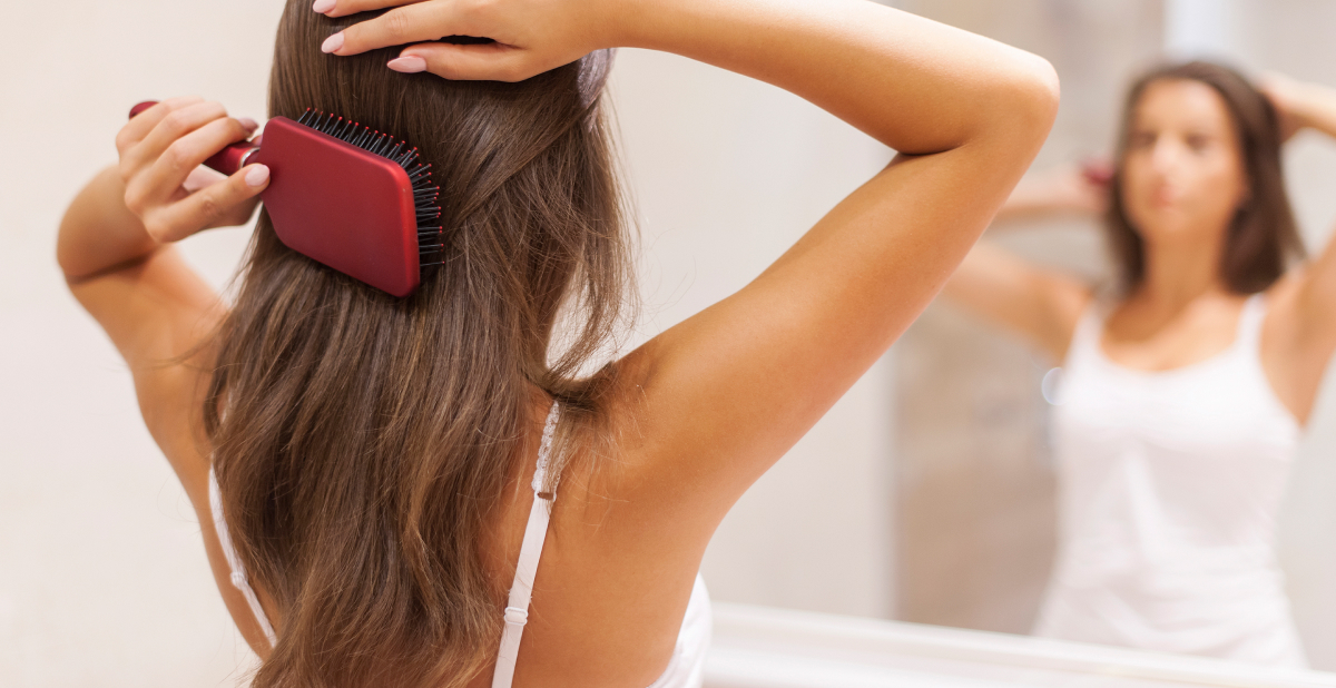 Mujer cepillándose el cabello frente al espejo para observar su aspecto y posible caída
