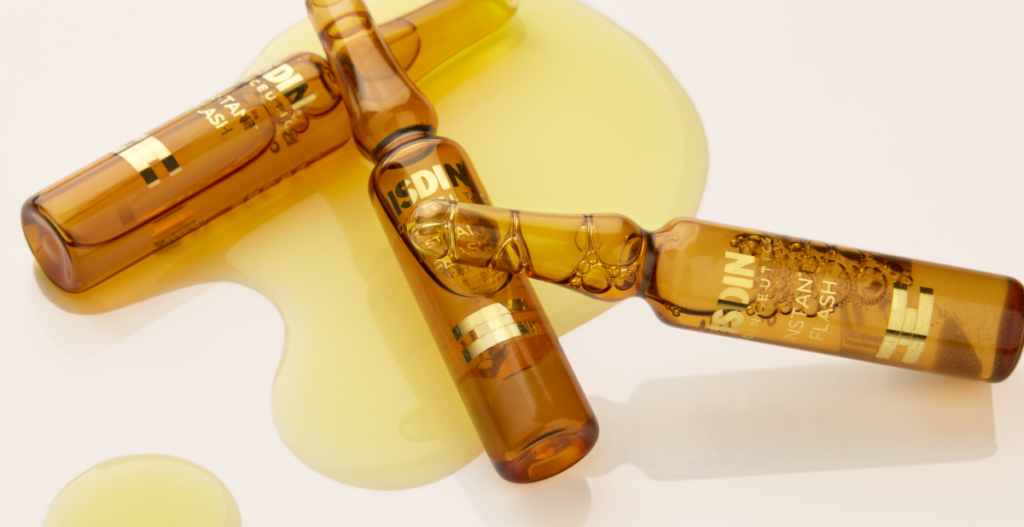 Ampollas ISDIN cosméticas abiertas con sérum dorado derramado sobre superficie, representando tratamiento intensivo de la piel