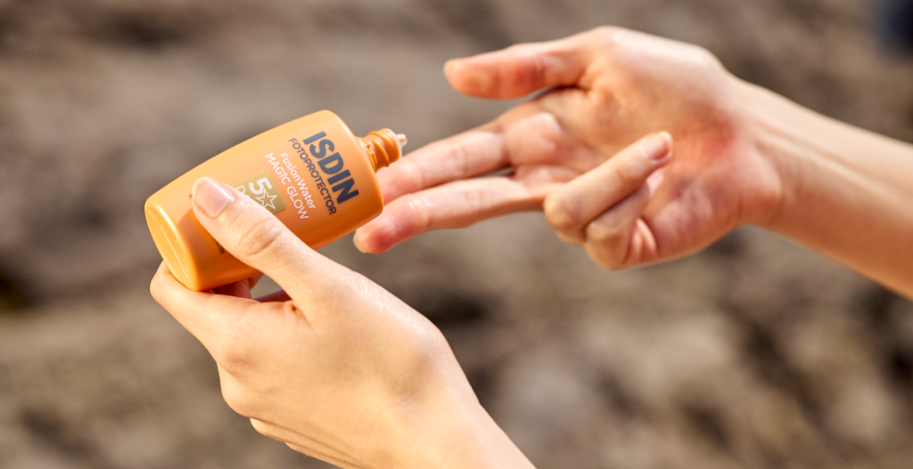 Manos aplicando protector solar líquido en los dedos para reaplicar de forma sencilla encima del maquillaje.