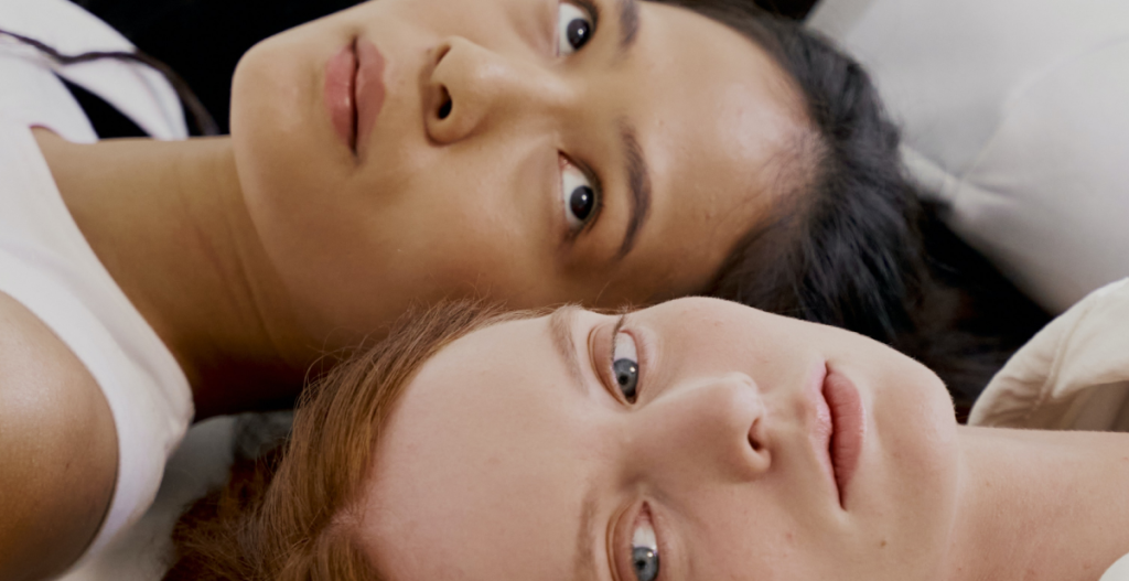 Dos mujeres recostadas, mirando hacia la cámara, mostrando la luminosidad y frescura en la zona del contorno de ojos.