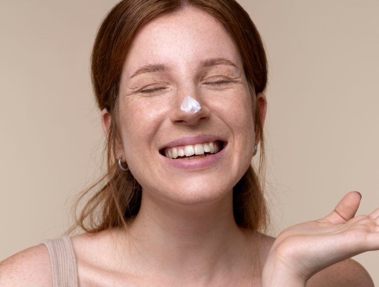 Mujer con piel seca sonriendo y con crema hidratante en la nariz durante su rutina de cuidado facial.