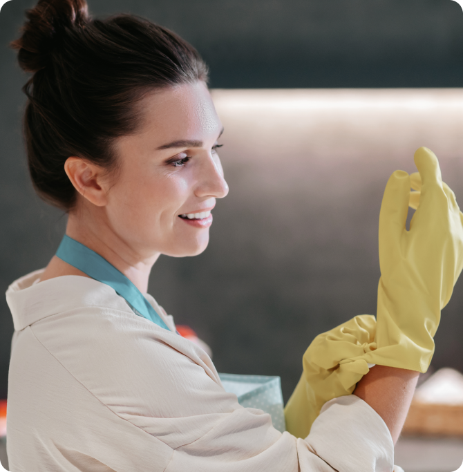 Mujer sonriente se coloca guantes amarillos para proteger sus uñas y manos durante tareas de limpieza. Representa hábito saludable de protección, prevención de quiebre y cuidado de la estructura ungueal.
