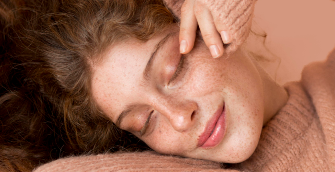 Mujer de piel con pecas y suéter rosa disfruta relajada con los ojos cerrados, transmitiendo bienestar y cuidado de la piel en otoño.