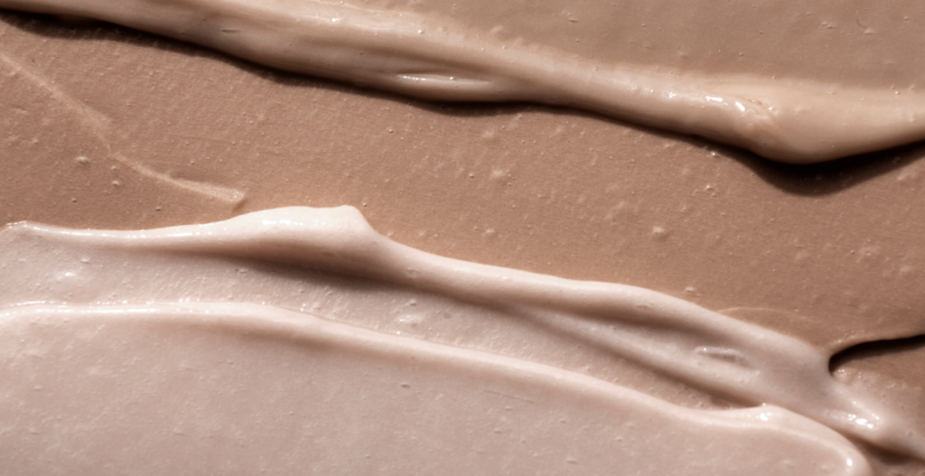 Texturas de cremas cosméticas en tonos beige y marrón extendidas sobre una superficie.