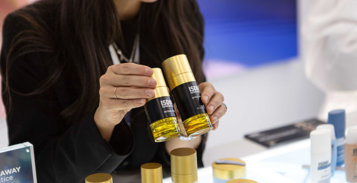 Profesional mostrando dos sérums ISDINCEUTICS con retinal en envases dorados, durante la presentación de novedades sobre la nueva era del retinal en IMCAS 2026.