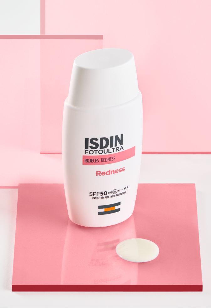 Envase de ISDIN Fotoultra Redness SPF 50 sobre fondo rosa, fotoprotector facial indicado para piel sensible con tendencia a rojeces y cuperosis.