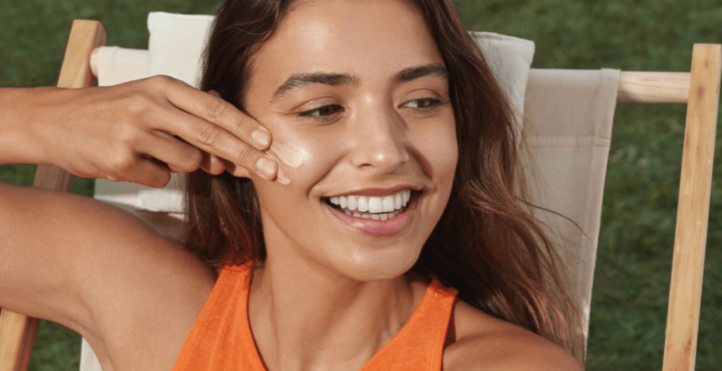 Mujer aplicando crema facial al sol durante una escapada de primavera para una piel luminosa y protegida