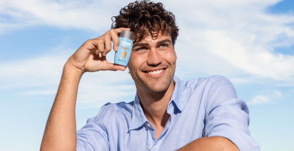 Hombre sonriendo mientras sostiene un fotoprotector facial ISDIN, producto de skincare para hombres con protección solar.