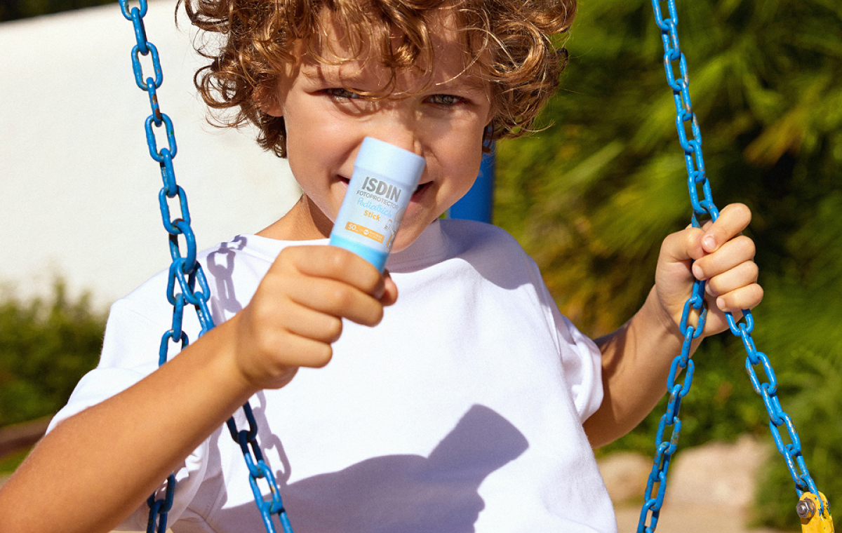 Niño en un columpio sosteniendo Pediatrics Stick SPF 50 de ISDIN durante un día soleado.