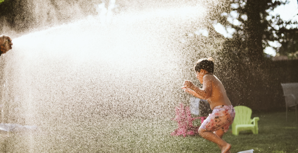Un niño corre entre el agua pulverizada de una manguera durante un día solead