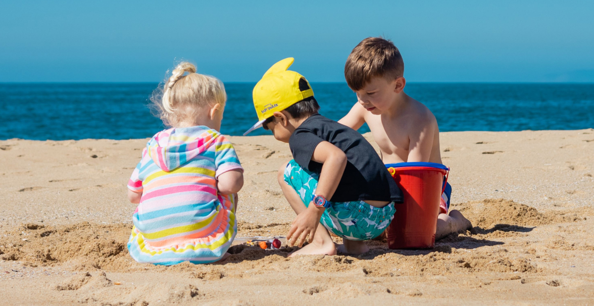 Tres niños juegan con cubos y juguetes en la arena de la playa junto al mar.