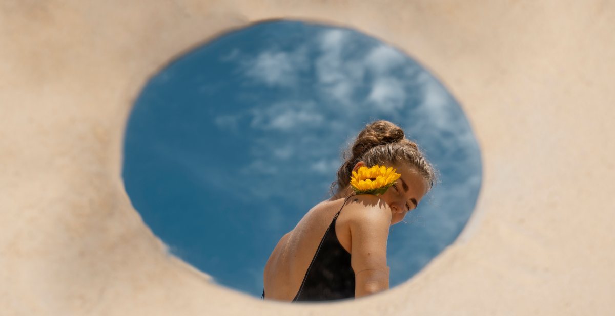 Mujer en primavera con una flor amarilla en el hombro, cielo azul de fondo y luz natural