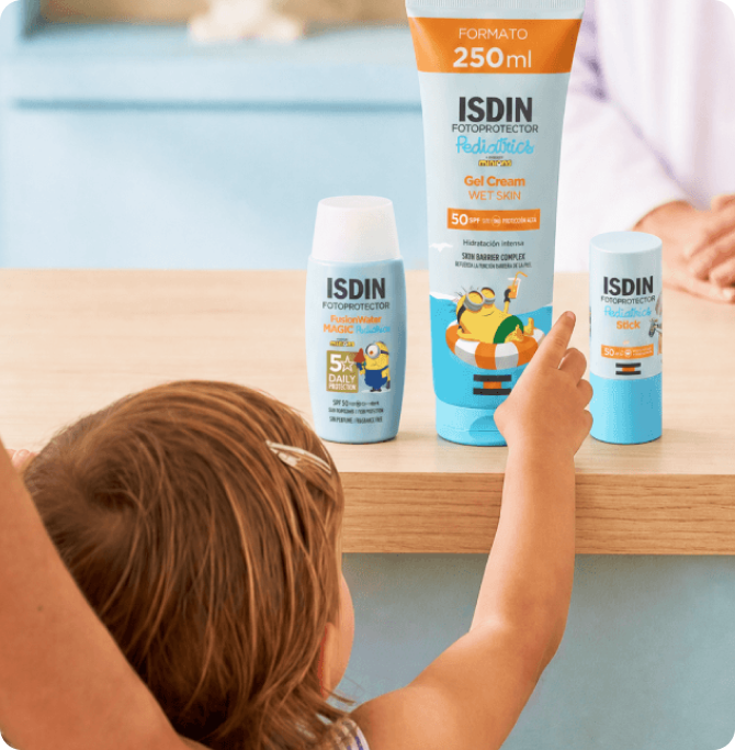 Niña eligiendo entre varios fotoprotectores ISDIN Pediatrics colocados sobre una mesa.
