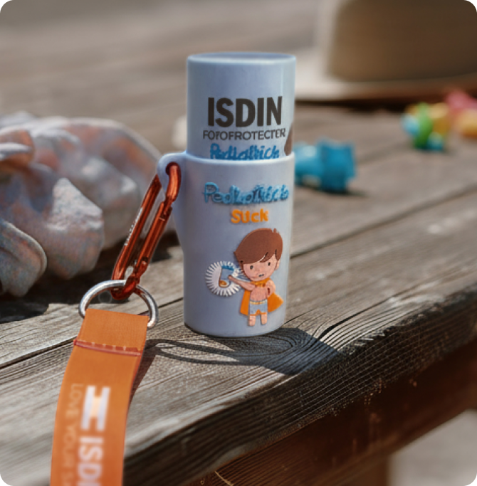 Pediatrics Stick SPF 50 de ISDIN con mosquetón sobre una mesa de madera al aire libre.