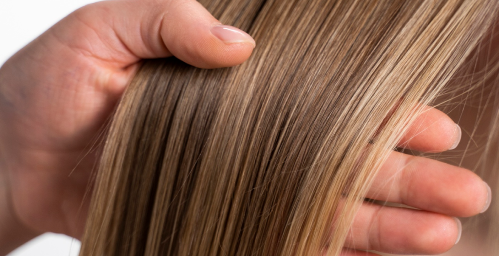 Mano sosteniendo un mechón de cabello liso con reflejos rubios.