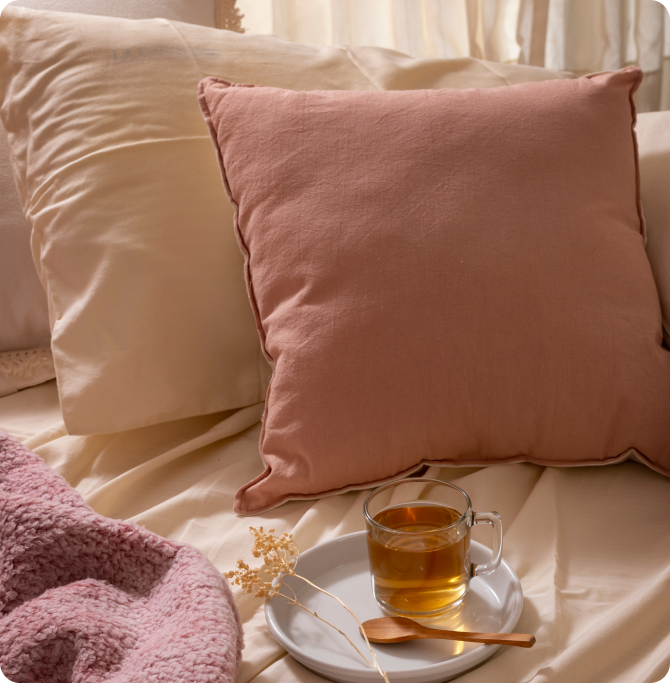 Cama con cojines beige y rosa y una taza sobre un plato.