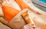 Primer plano de una mujer en bikini naranja recostada al borde de una piscina, sujetando ISDIN Body Glow SPF 30 sobre su abdomen luminoso y tonificado.