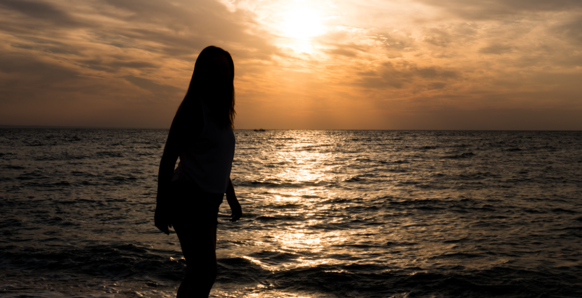 Mujer en silueta frente al mar al atardecer, disfrutando de un momento de calma tras un día de playa