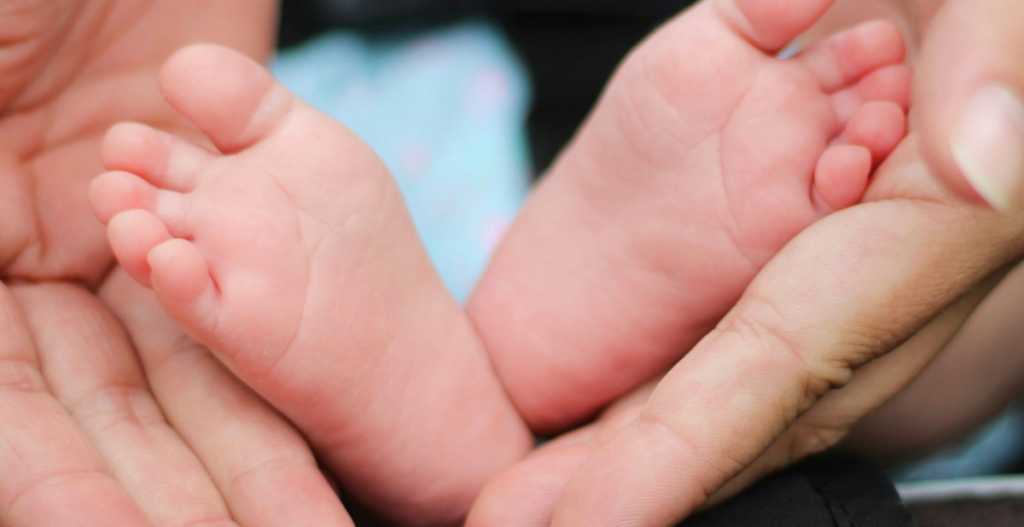 Primer plano de los pies de un recién nacido sostenidos con delicadeza por las manos de un adulto.