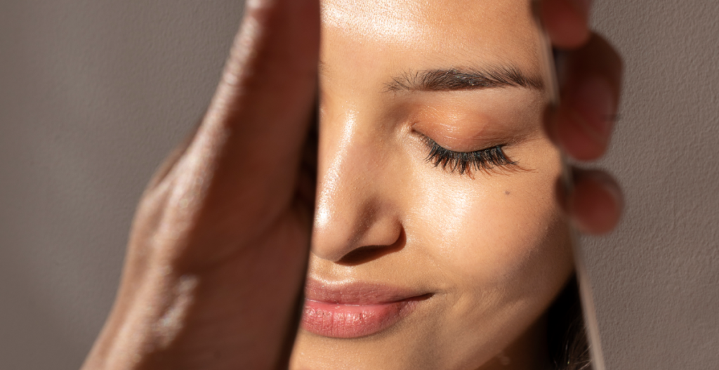Rostro femenino relajado y luminoso, reflejado en un espejo, tras seguir una rutina facial post-playa