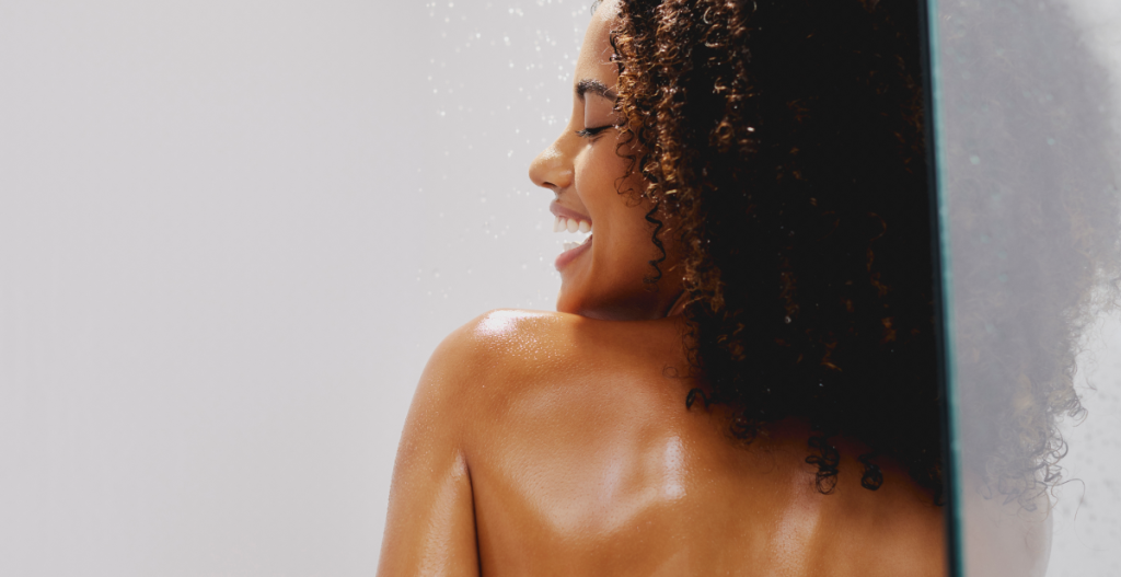 Mujer sonriente bajo la ducha, disfrutando de la hidratación tras un día de sol y salitre