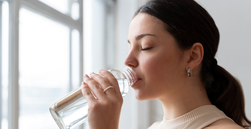 Mujer bebiendo agua de una botella, gesto clave para hidratar la piel